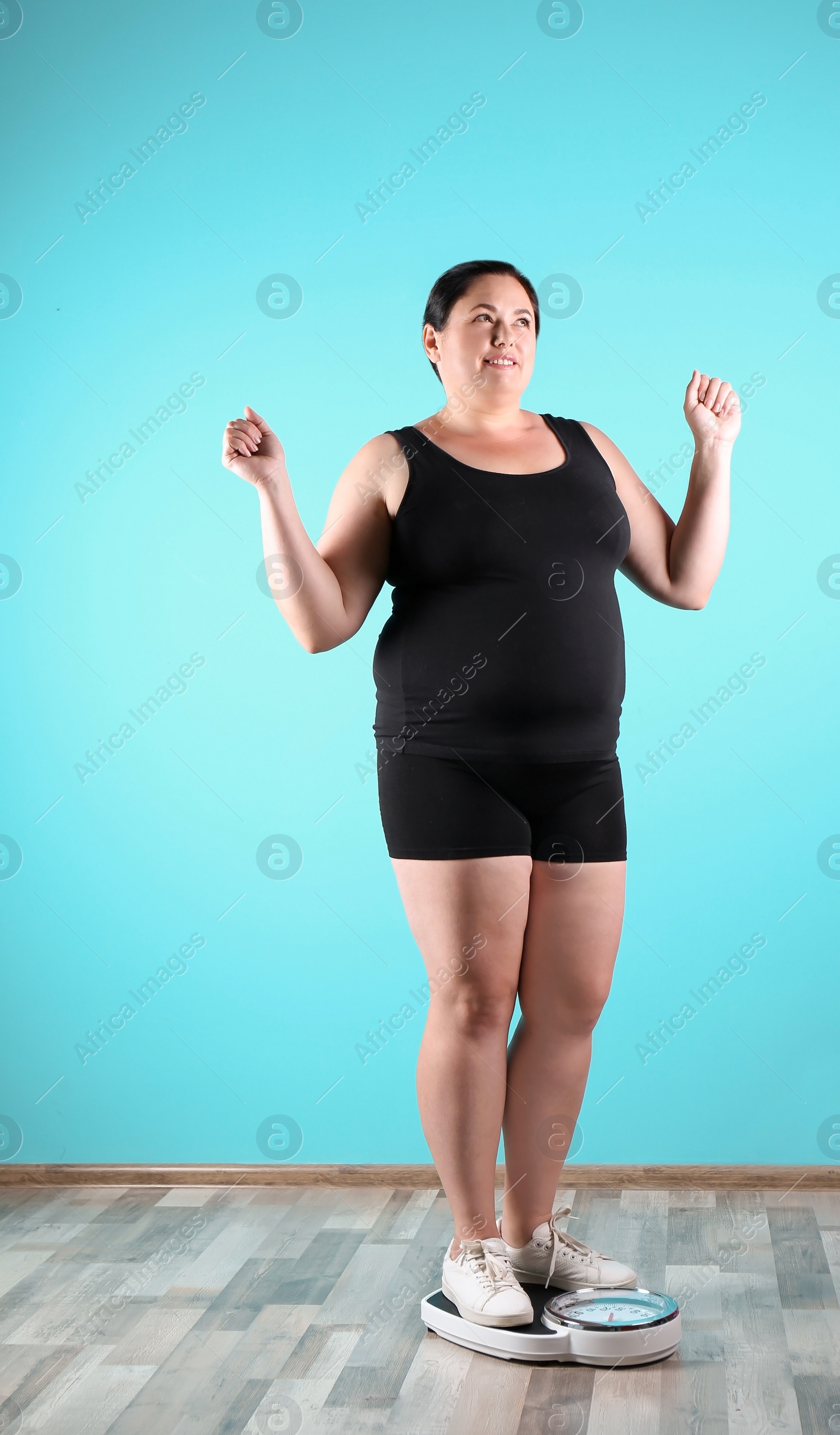 Photo of Overweight woman in sportswear using scales near color wall