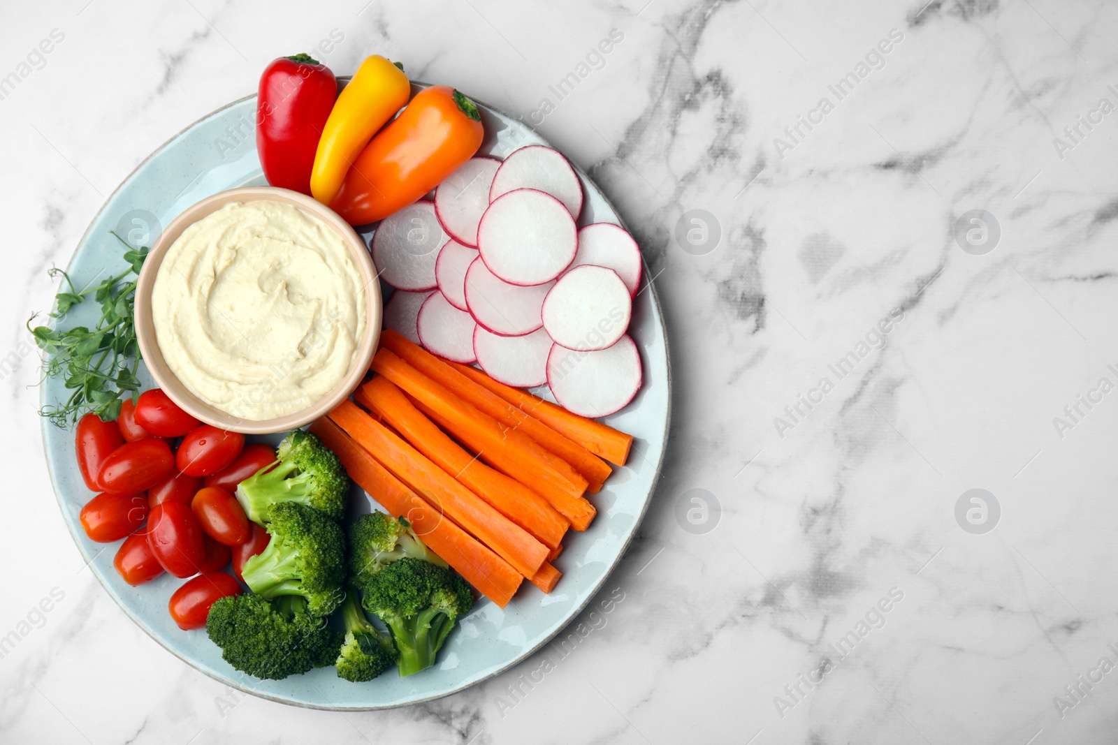 Photo of Plate with delicious hummus and fresh vegetables on white marble table, top view