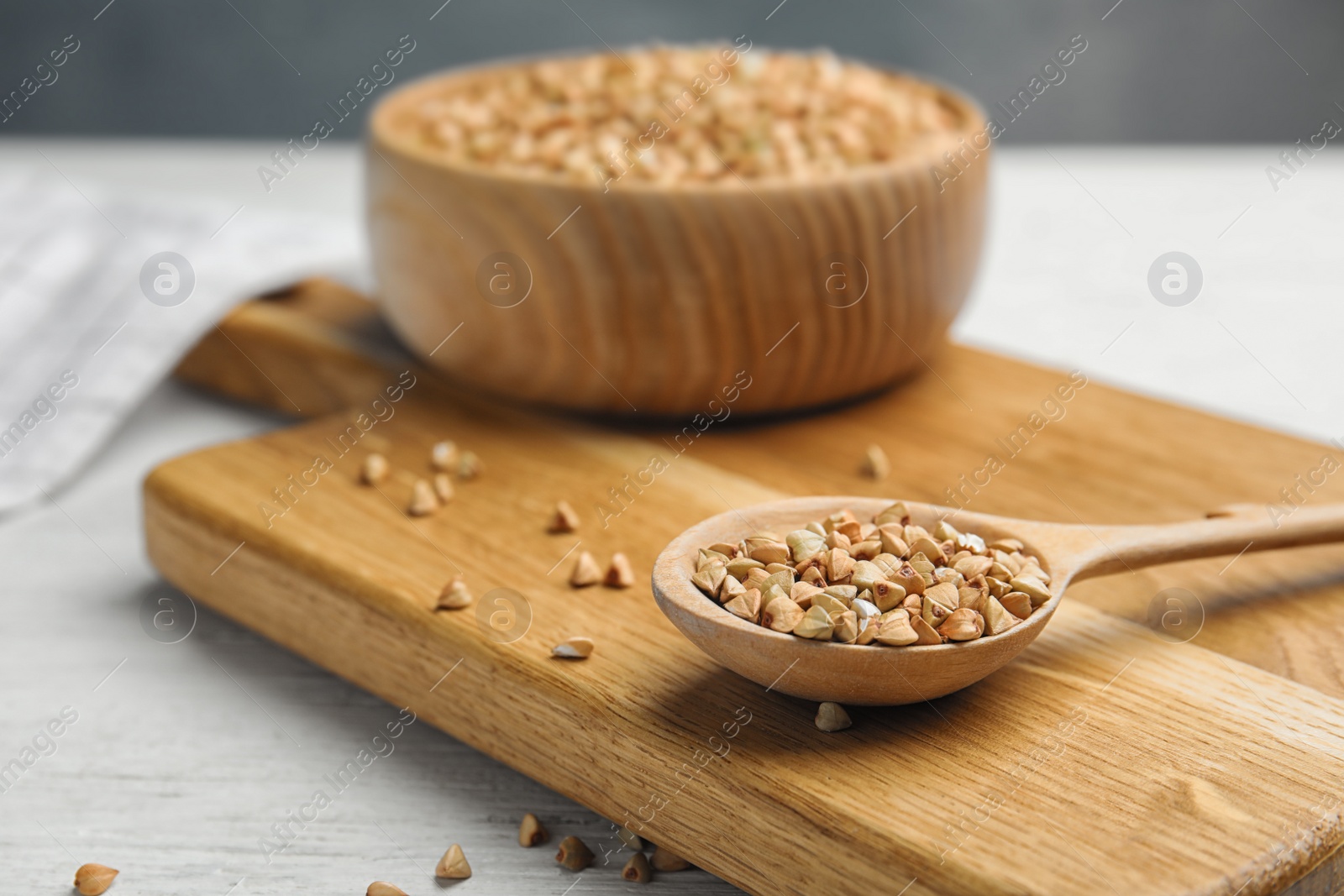 Photo of Uncooked green buckwheat grains in spoon on white wooden table, closeup. Space for text