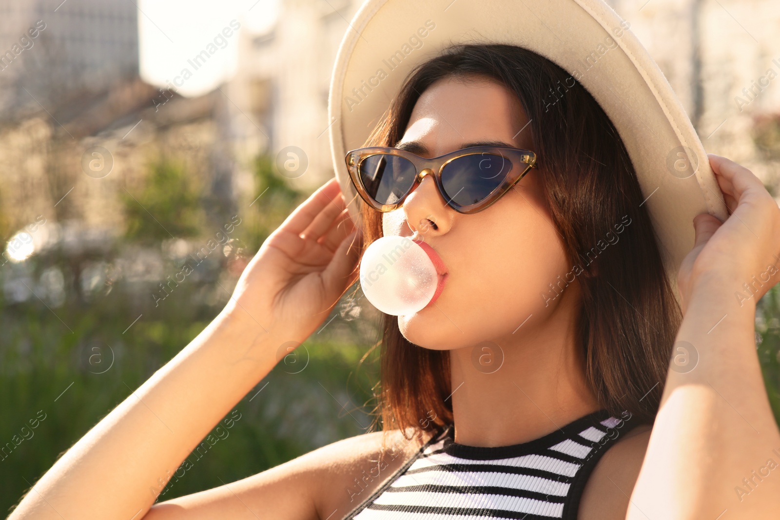 Photo of Beautiful woman in stylish sunglasses blowing gum outdoors on sunny day