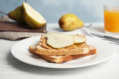 Photo of Slice of bread with peanut butter and pear on white wooden table