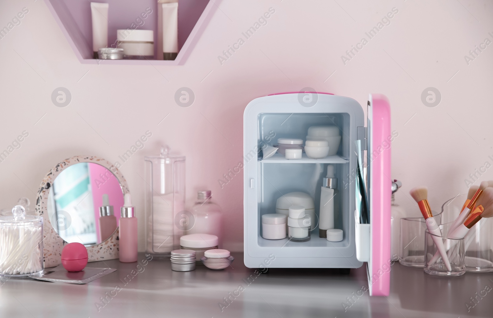 Photo of Mini fridge with cosmetic products on grey vanity table indoors