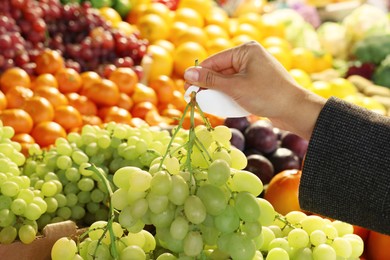 Photo of Woman holding fresh grapes near fruit counter at market, closeup