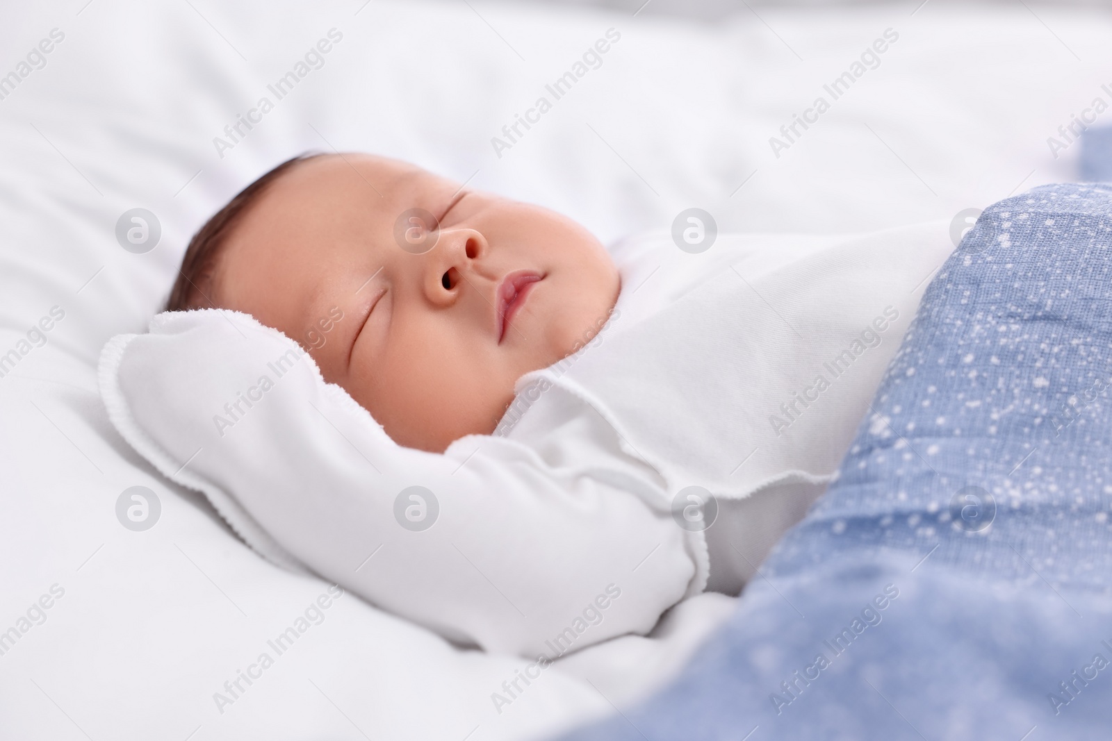 Photo of Cute newborn baby sleeping under blue blanket on bed, closeup