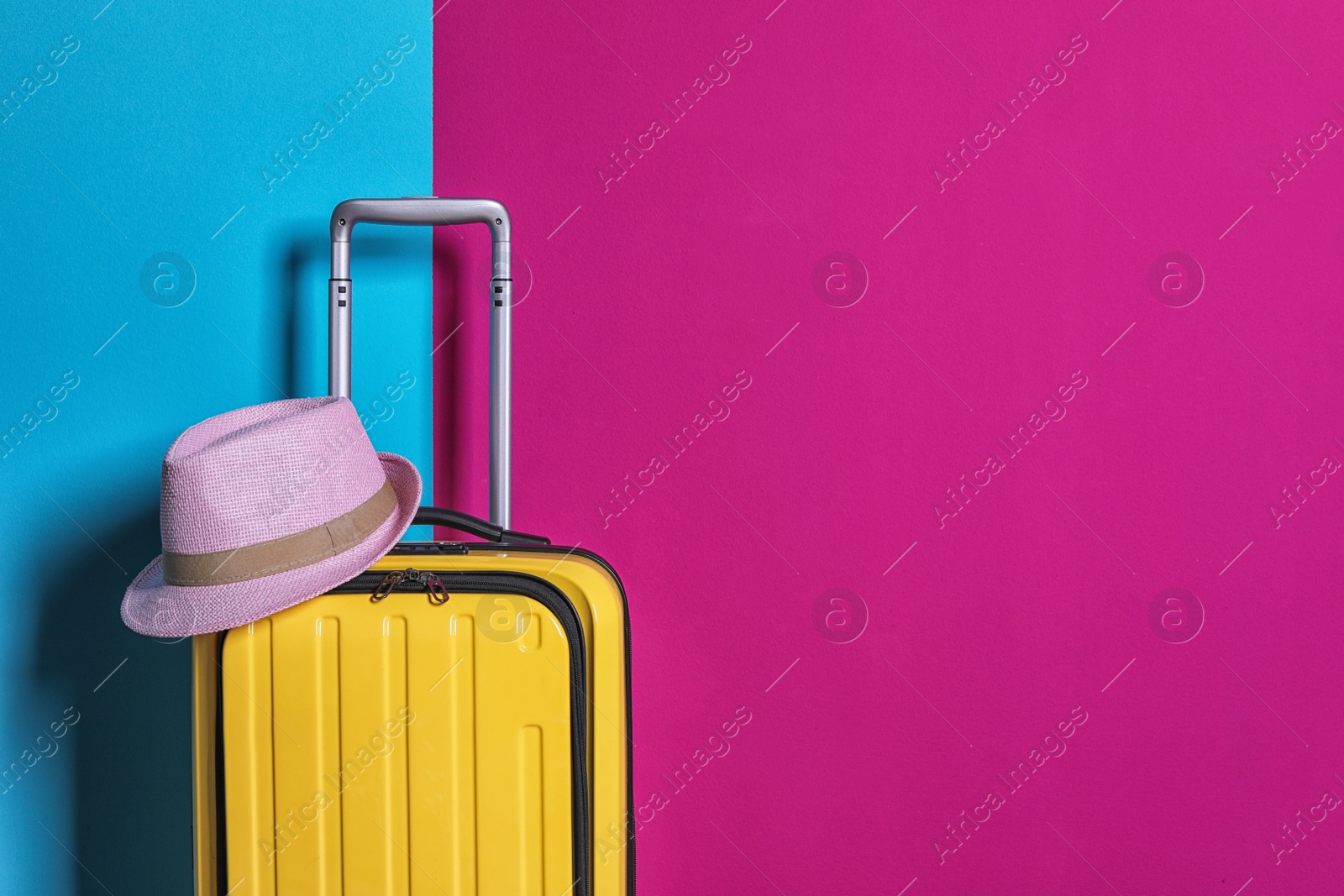 Photo of Bright yellow suitcase with hat on color background