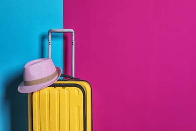 Bright yellow suitcase with hat on color background