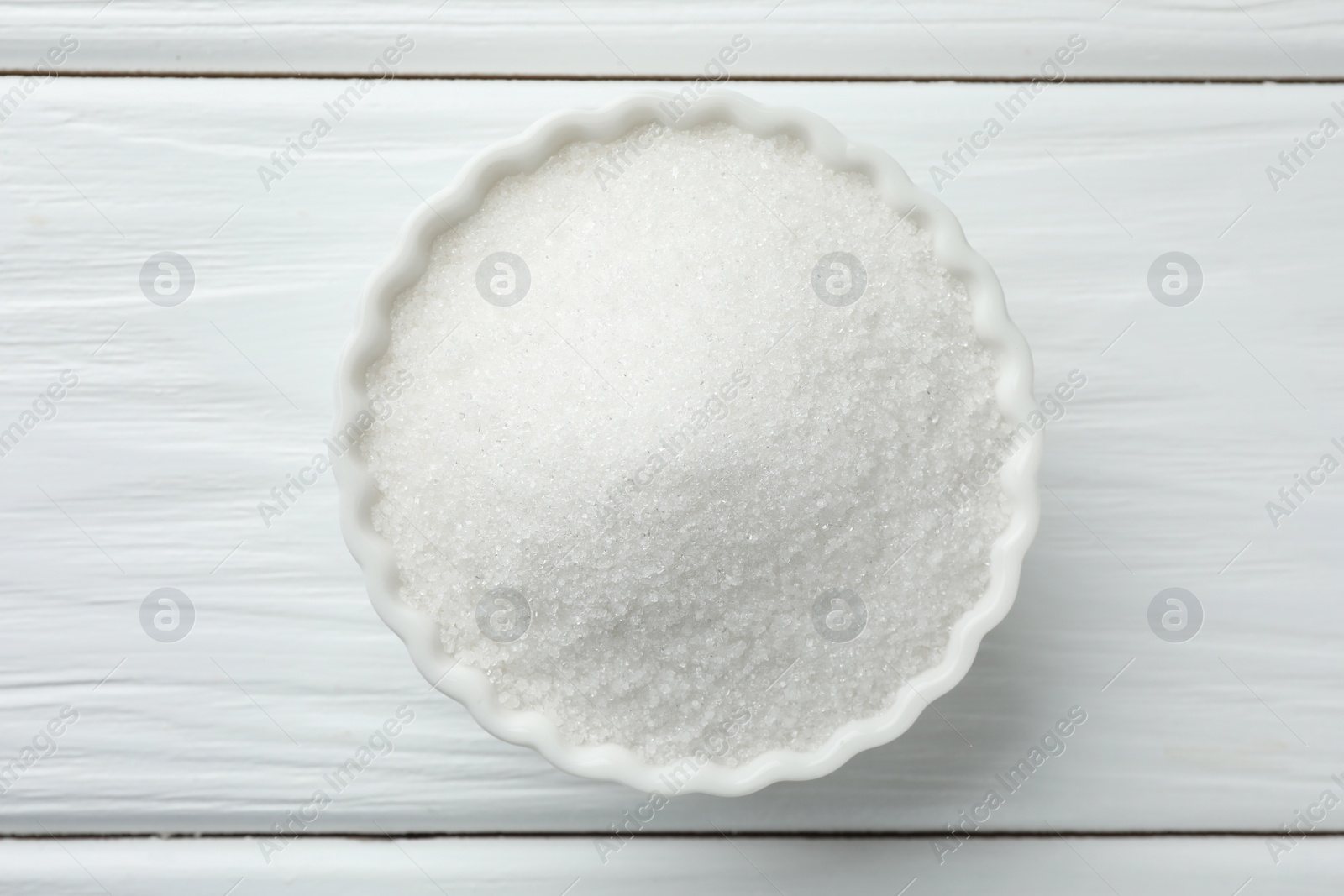 Photo of Granulated sugar in bowl on white wooden table, top view