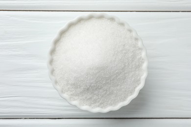 Photo of Granulated sugar in bowl on white wooden table, top view
