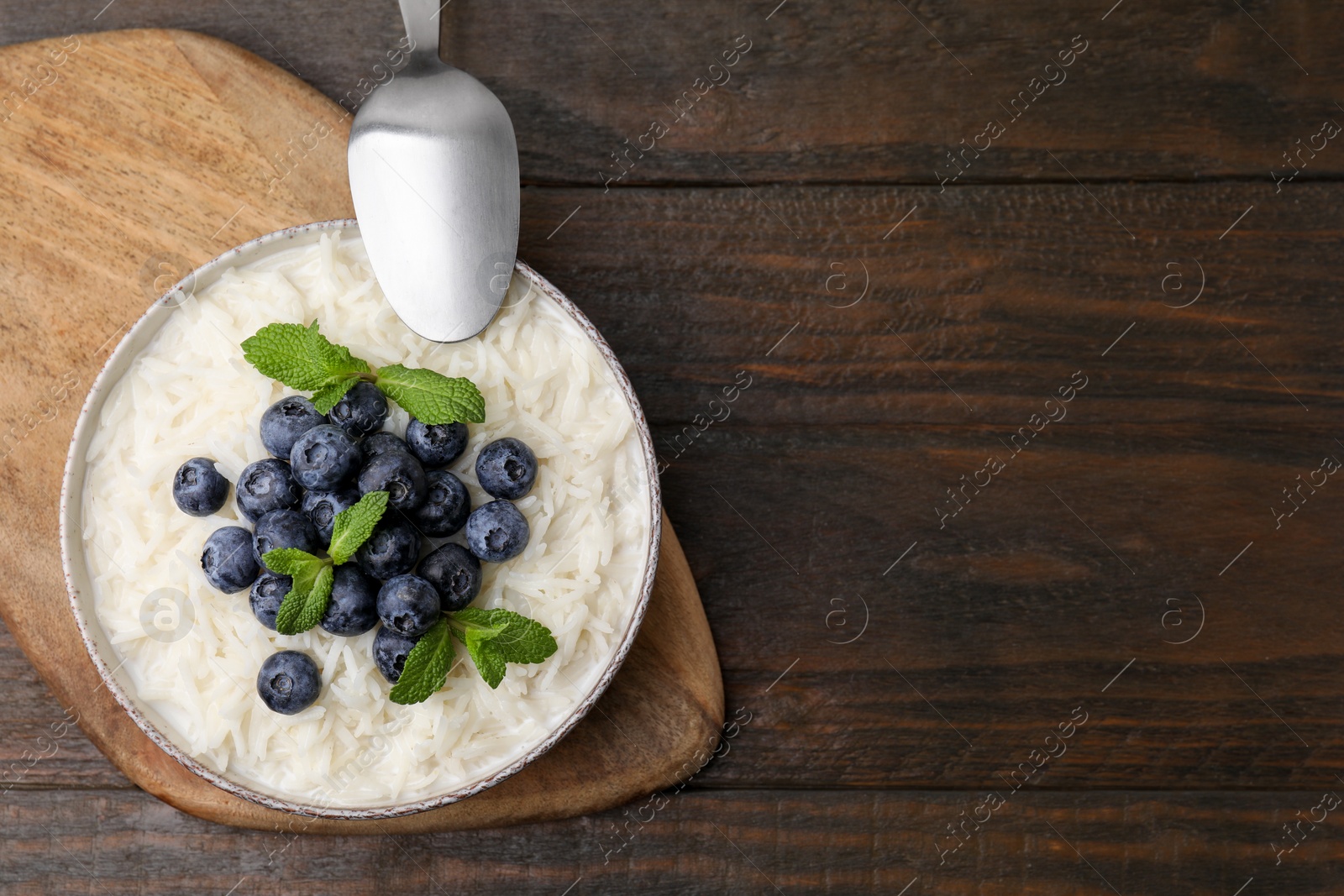 Photo of Bowl of delicious rice porridge with blueberries and mint served on wooden table, top view. Space for text