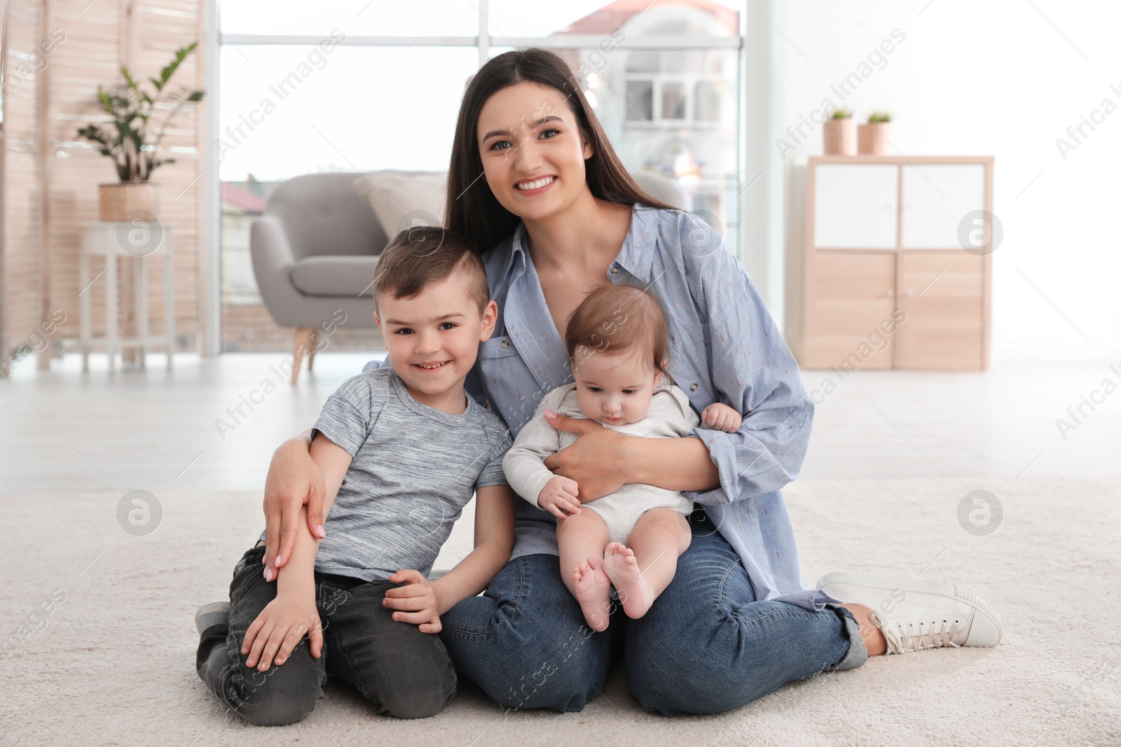 Photo of Young mother with her children sitting together on floor at home