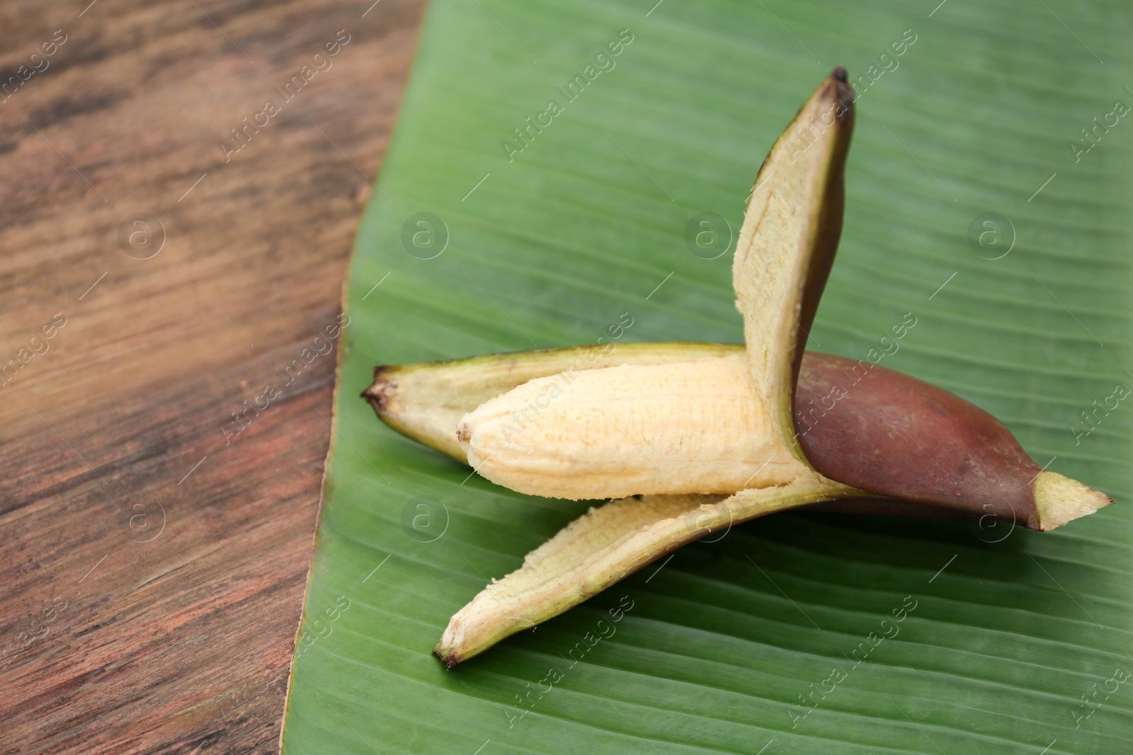 Photo of Delicious purple banana and fresh leaf on wooden table, closeup. Space for text