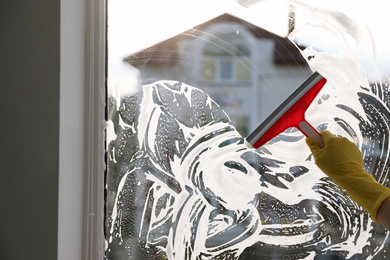 Woman cleaning window with squeegee indoors, closeup