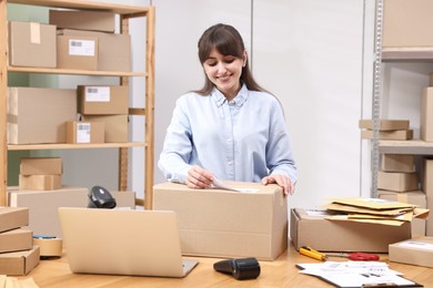 Photo of Parcel packing. Post office worker sticking barcode on box at wooden table indoors