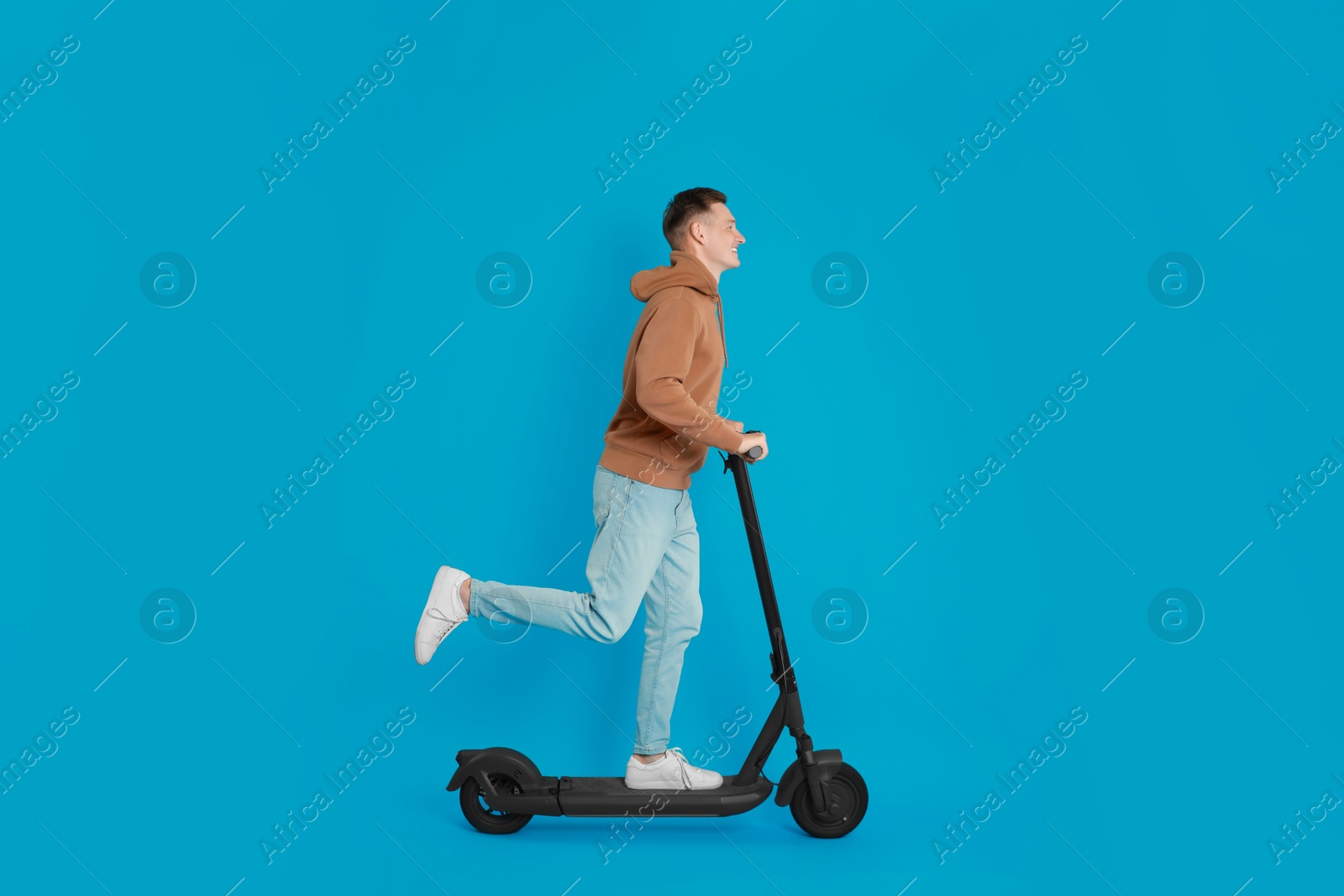 Photo of Young man riding modern electric kick scooter on light blue background