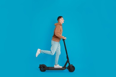 Young man riding modern electric kick scooter on light blue background