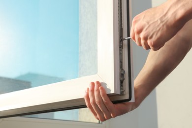 Photo of Worker adjusting installed window with screwdriver indoors, closeup