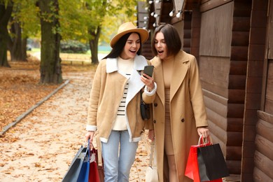 Special Promotion. Emotional young women with shopping bags and smartphone on city street