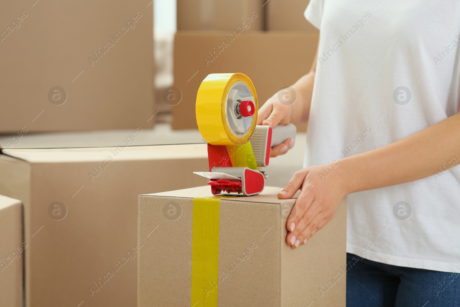 Photo of Woman applying adhesive tape on box with dispenser indoors, closeup