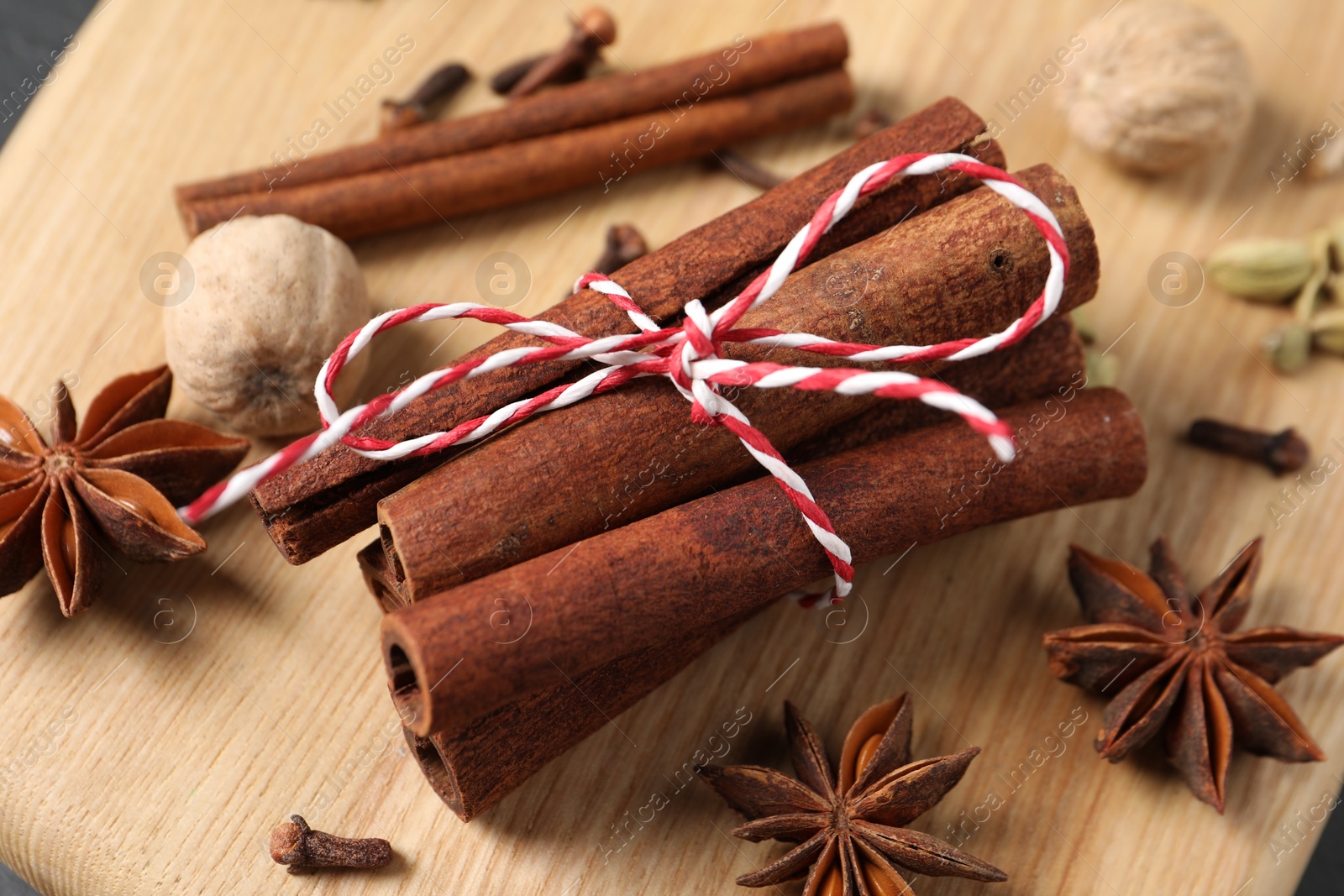 Photo of Cinnamon sticks and other spices on wooden board, closeup