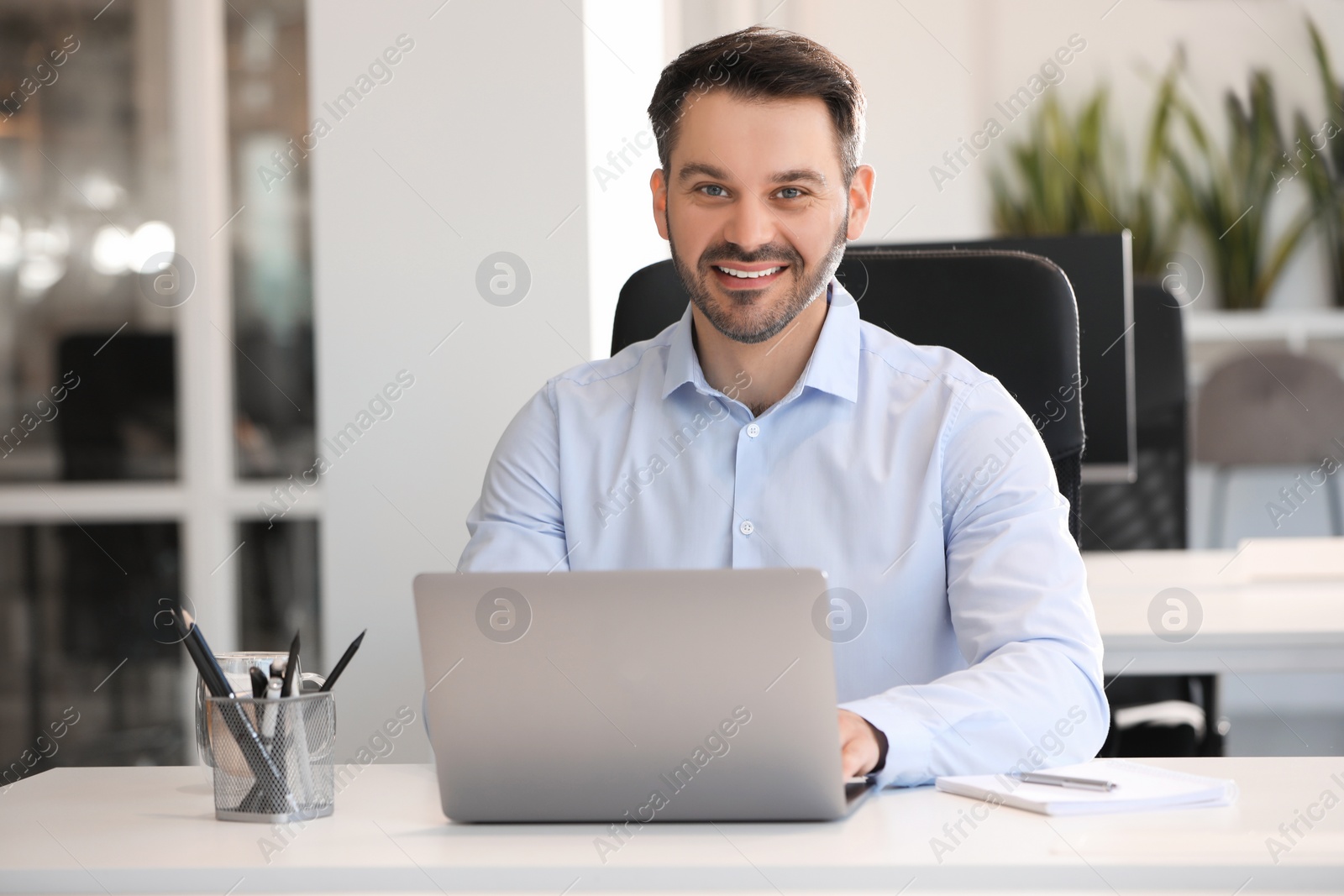 Photo of Happy man using modern laptop at white desk in office