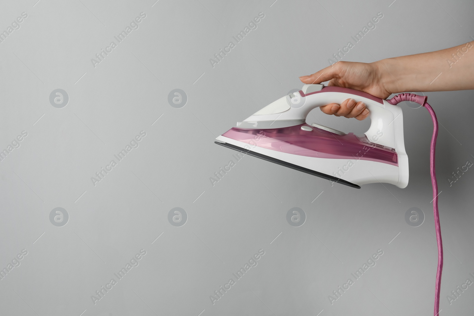 Photo of Woman holding modern iron on light grey background, closeup. Space for text