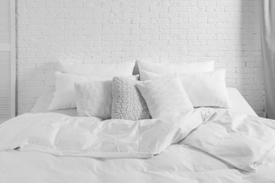 Photo of Large comfortable bed with pillows and blanket near white brick wall indoors. Stylish interior