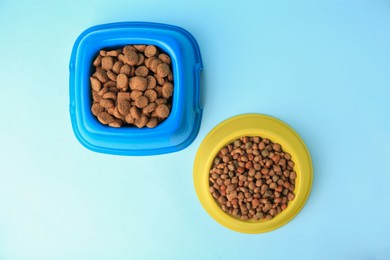 Dry pet food in feeding bowls on light blue background, flat lay