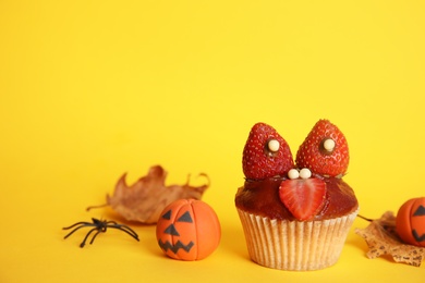 Photo of Delicious cupcake decorated as monster on yellow background. Halloween treat