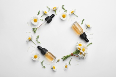 Photo of Composition with chamomile flowers and cosmetic bottles of essential oil on white background, top view. Space for text