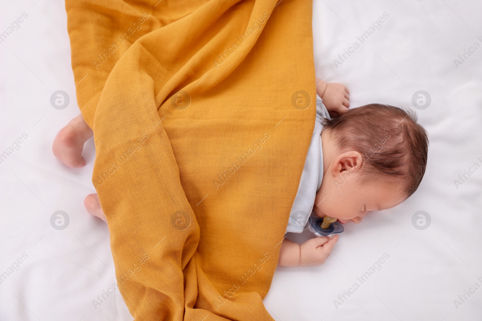 Photo of Cute newborn baby with pacifier sleeping under blanket on bed, top view