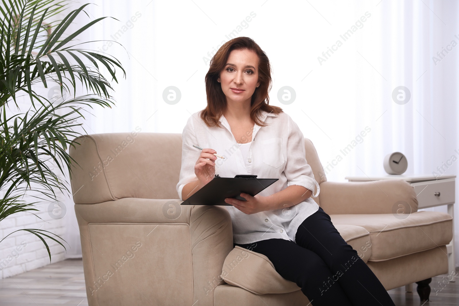 Photo of Portrait of psychotherapist with clipboard on sofa in office