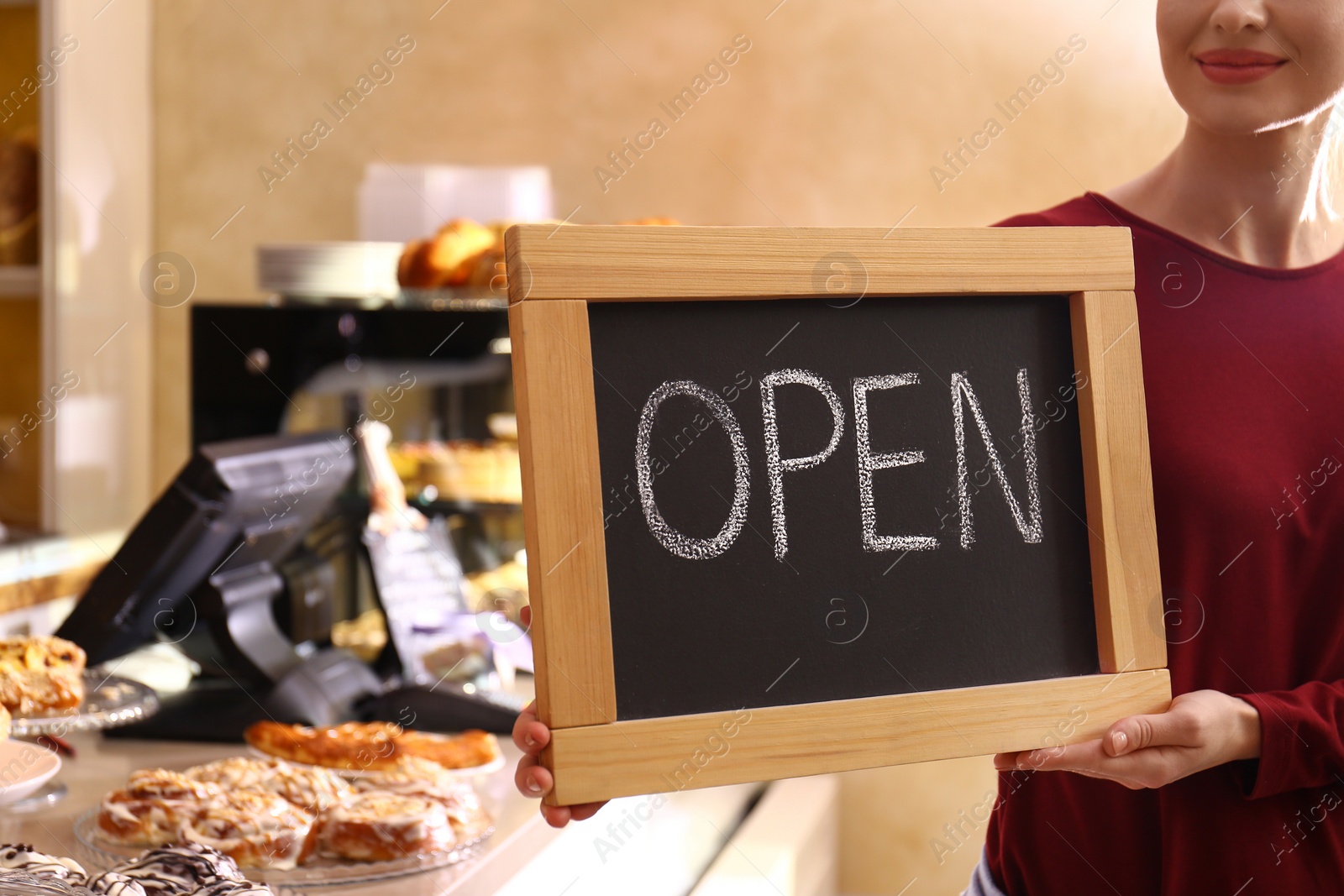 Photo of Female business owner holding OPEN sign in bakery, closeup