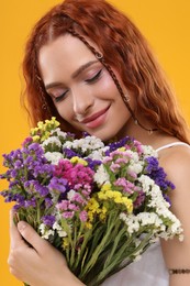 Photo of Beautiful young hippie woman with bouquet of colorful flowers on orange background, closeup