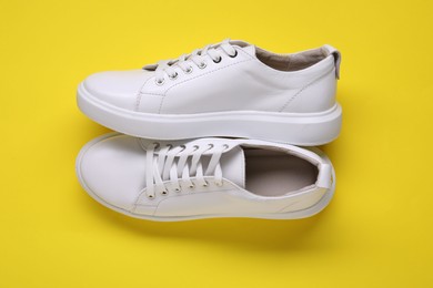 Photo of Pair of stylish white sneakers on yellow background, top view