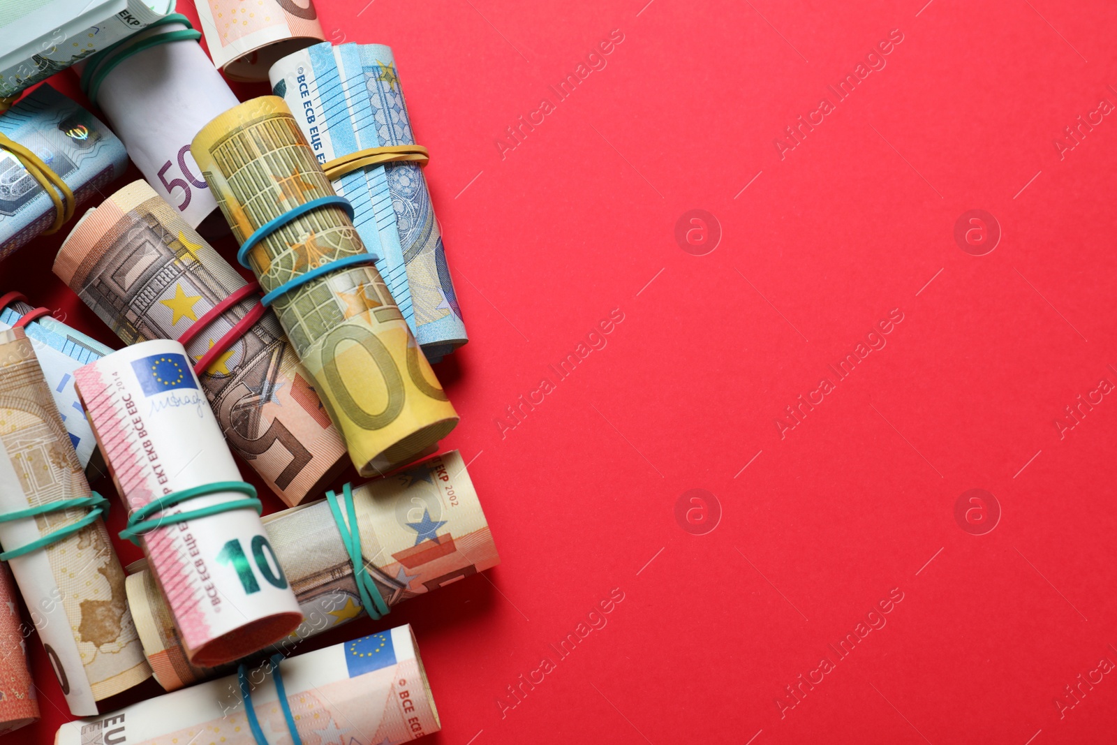 Image of Rolled money with rubber band on red background, flat lay. Space for text