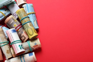 Rolled money with rubber band on red background, flat lay. Space for text