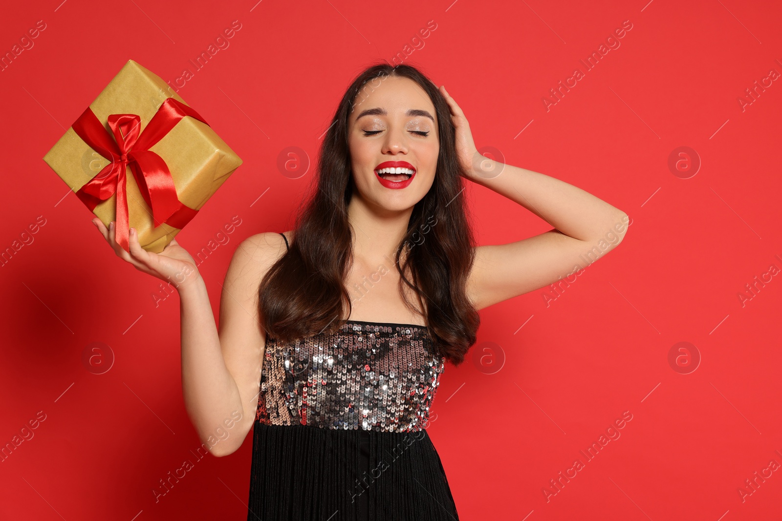 Photo of Beautiful young woman with Christmas gift on red background