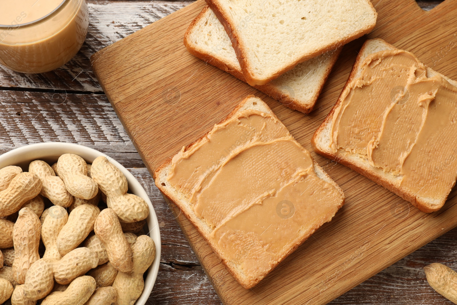 Photo of Tasty peanut butter sandwiches and peanuts on wooden table, flat lay