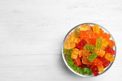 Photo of Bowl with delicious bright jelly bears on white wooden table, top view. Space for text