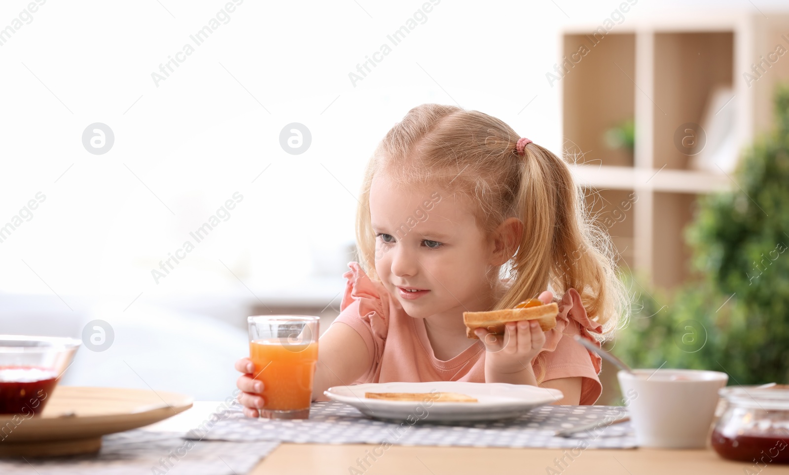 Photo of Cute little girl eating tasty toasted bread with jam at table