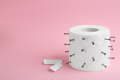 Roll of toilet paper with nails and suppositories on pink background, space for text. Hemorrhoid problems