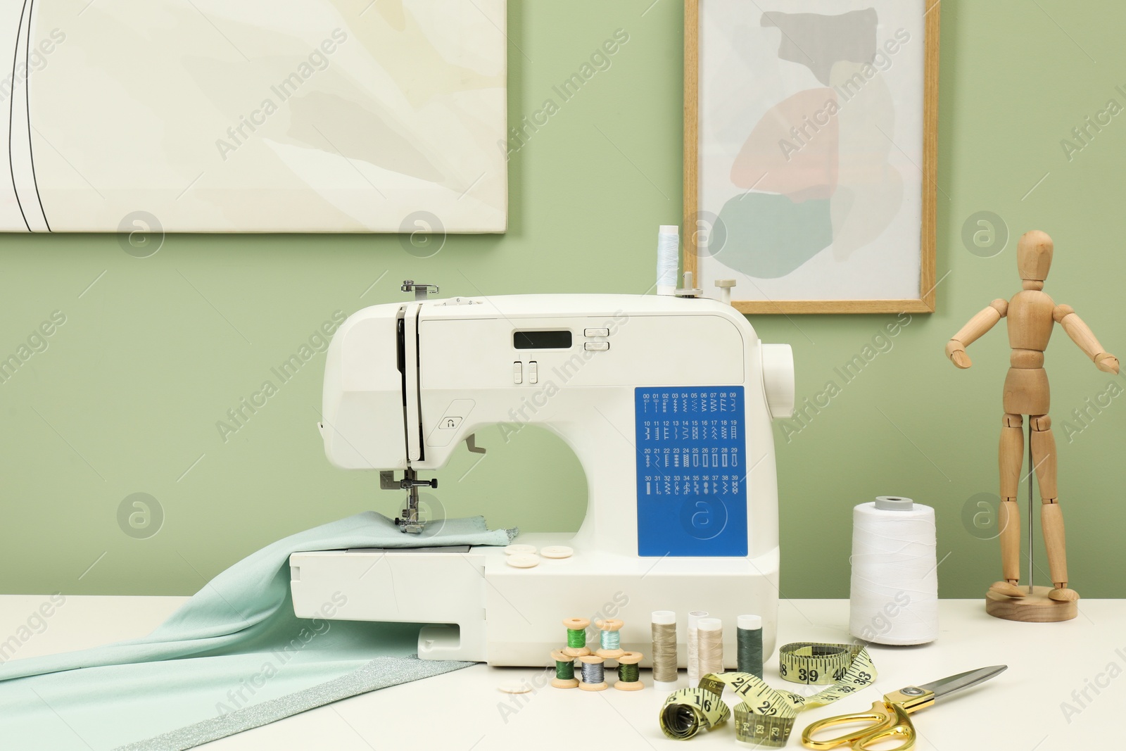 Photo of Modern sewing machine with cloth and craft accessories on white table near light green wall