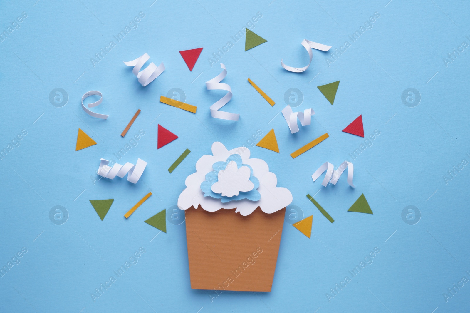 Photo of Paper cupcake and confetti on light blue background, flat lay