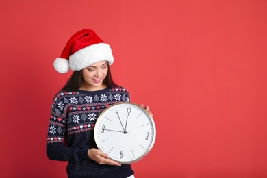 Young beautiful woman in Santa hat holding big clock on color background. Christmas celebration