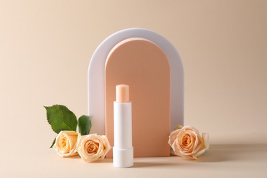 Stylish presentation of lip balm with rose flowers on beige background