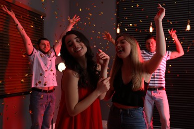 Happy friends and falling confetti in dark room