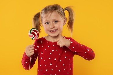 Happy girl pointing at lollipop on orange background