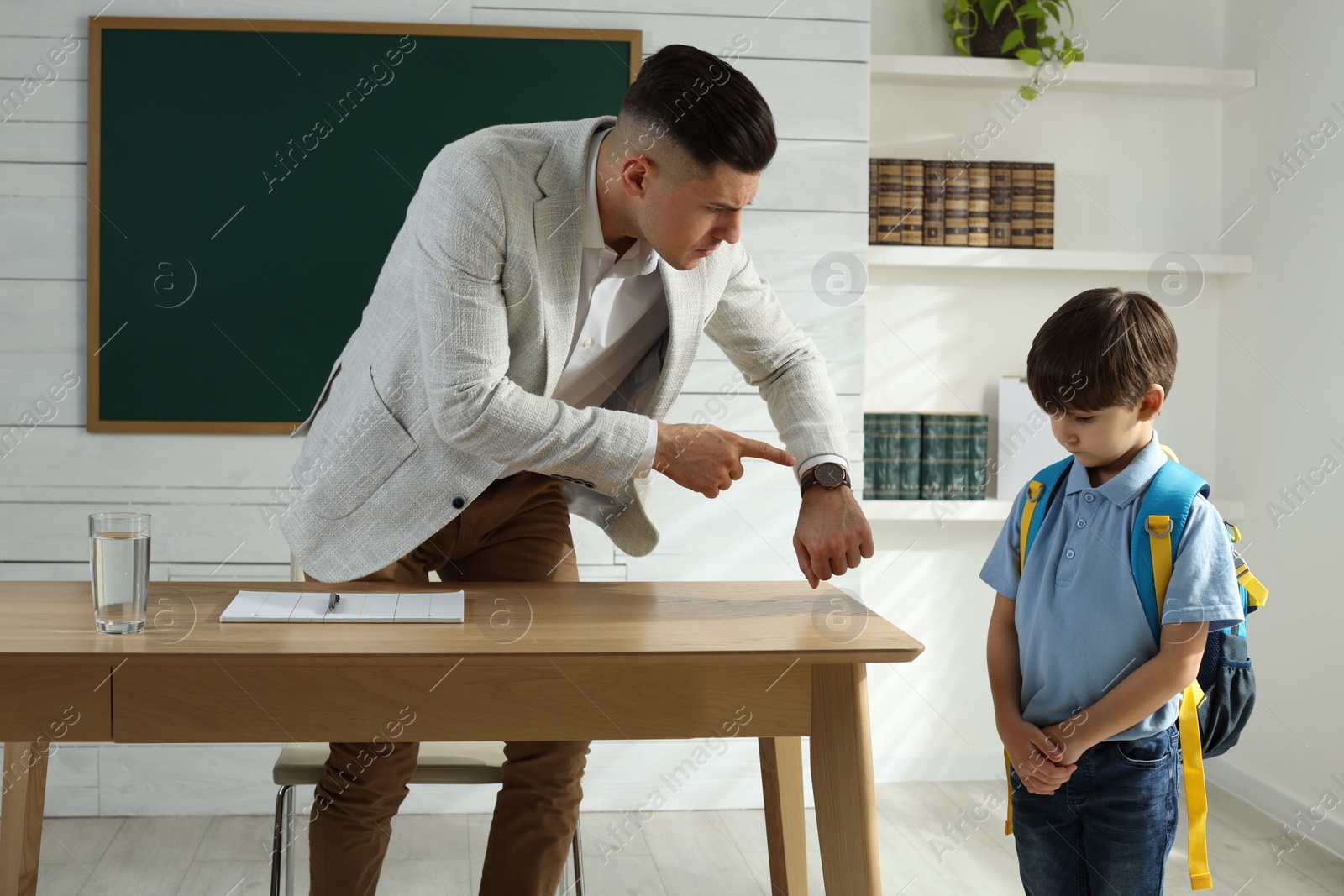 Photo of Teacher pointing on wrist watch while scolding pupil for being late in classroom