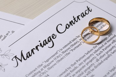 Photo of Marriage contracts and gold rings on light wooden table, closeup