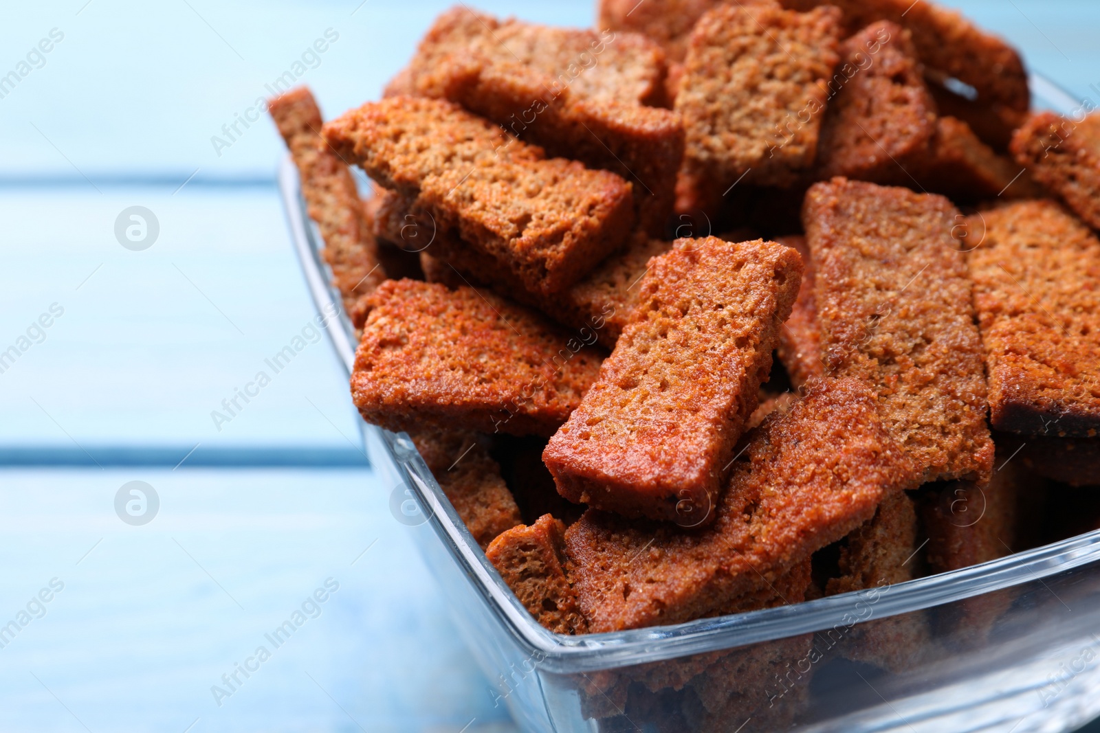 Photo of Crispy rye rusks in bowl on light blue wooden table, closeup